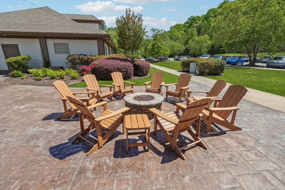 A circle of Adirondack chairs around a stone fire pit on a stamped-concrete patio outside the clubhouse
