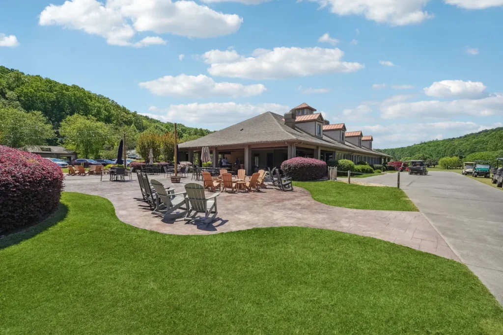Outdoor clubhouse patio with dining tables, landscaped lawn, and wooded foothills